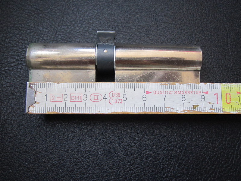 Im Bild ist ein Schließzylinder abgebildet, dessen länger mithilfe eines Zollstockes ausgemessen wird