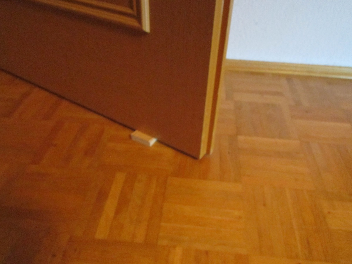 Ein Holzkeil liegt unter einer Tür und schützt siese davor zuzufallen